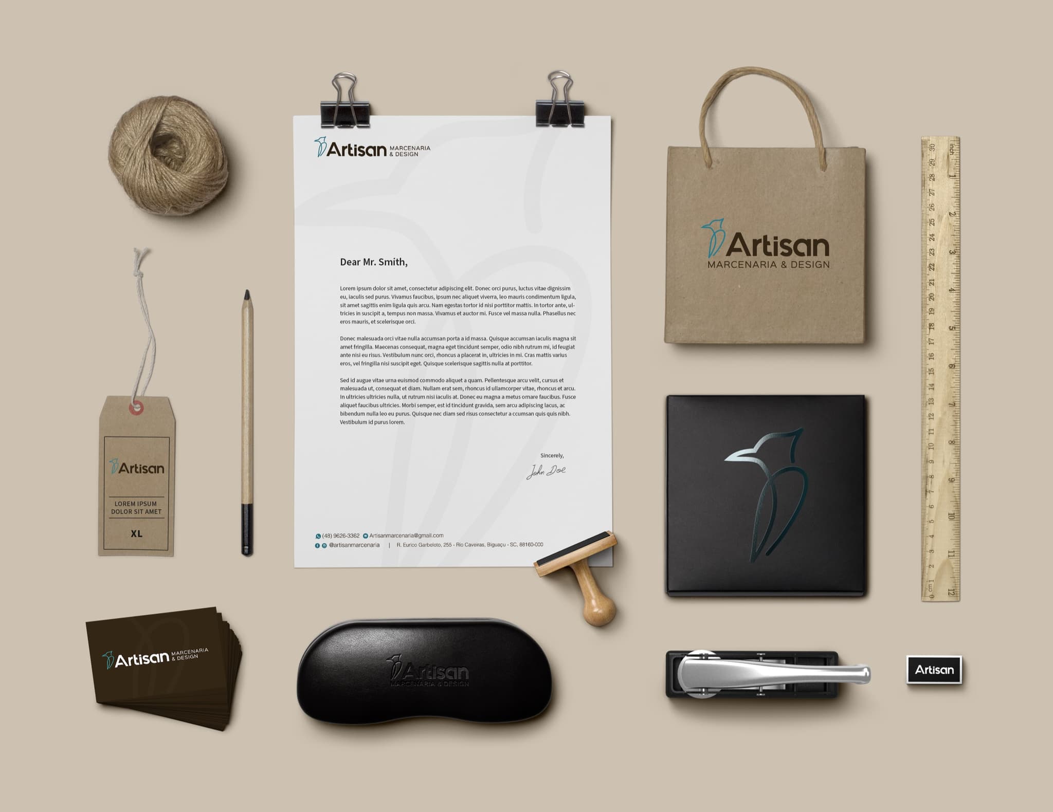 Papelaria completa da Artisan Marcenaria disposta sobre fundo bege: papel timbrado, sacola kraft, etiqueta, cartões, caixa preta com o pica-pau em verniz e carimbo