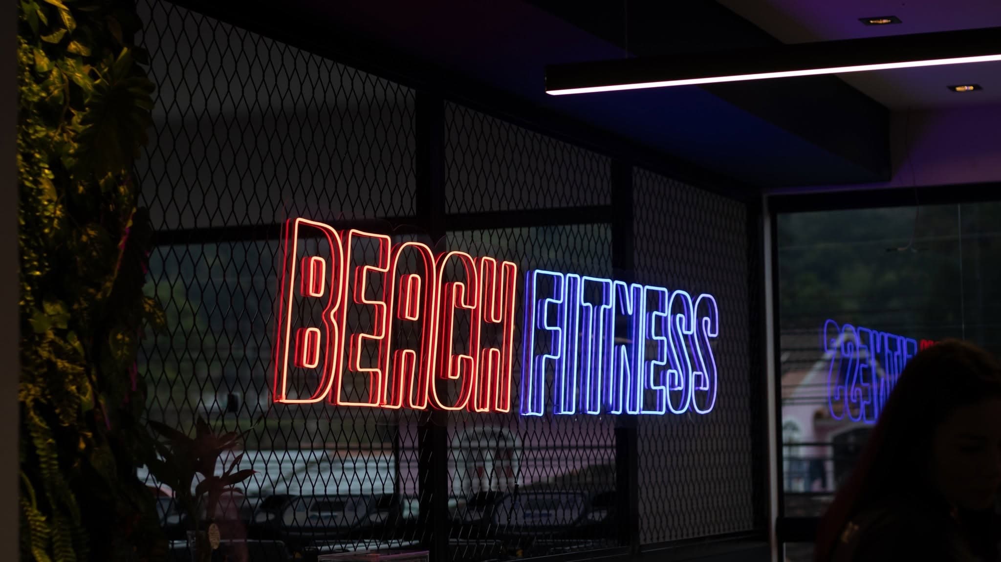 Letreiro em neon vermelho e azul com o nome Beach Fitness na parede da academia