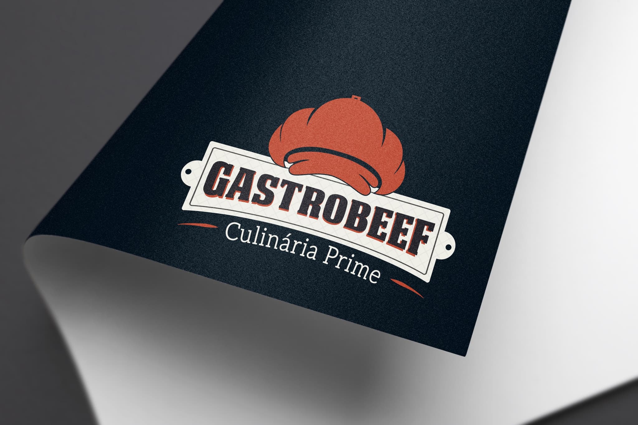 Logotipo GastroBeef impresso em papel azul-marinho com a ponta enrolada, a touca vermelha destacada sobre a chapa clara