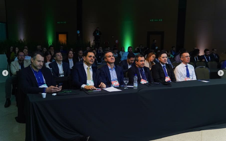 Mesa de autoridades na primeira fila do auditório da ExpoJud, com crachás do evento e a iluminação cênica verde ao fundo