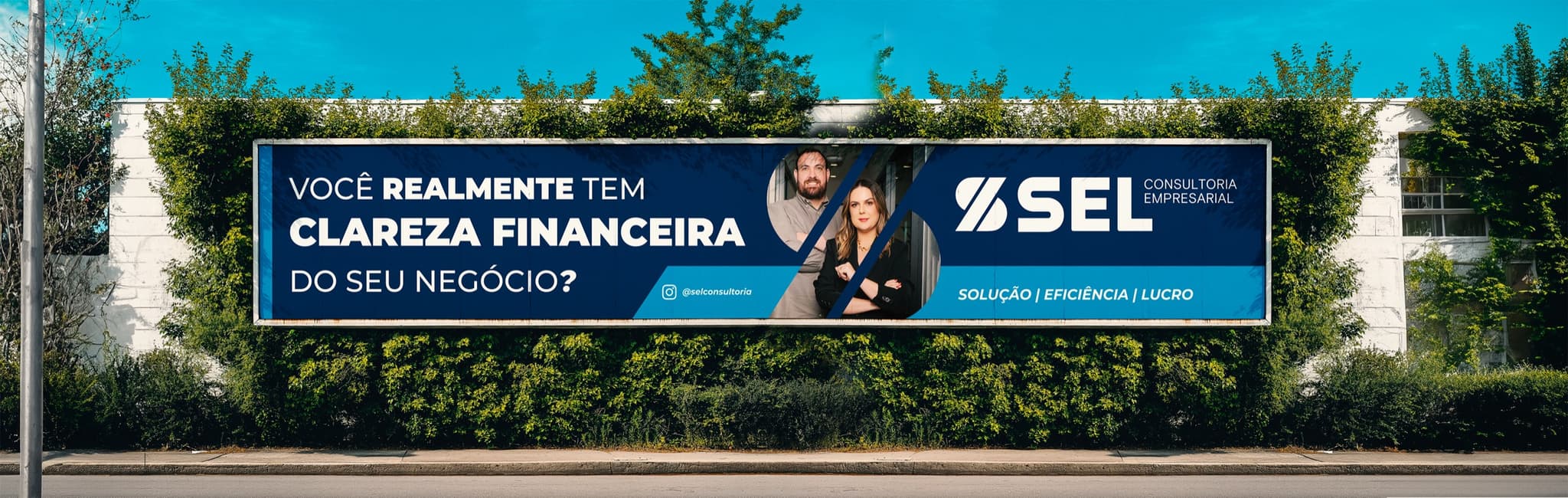 Outdoor 18x3 da SEL Consultoria sobre um muro verde, com a pergunta “Você realmente tem clareza financeira do seu negócio?” e os dois sócios ao lado da marca