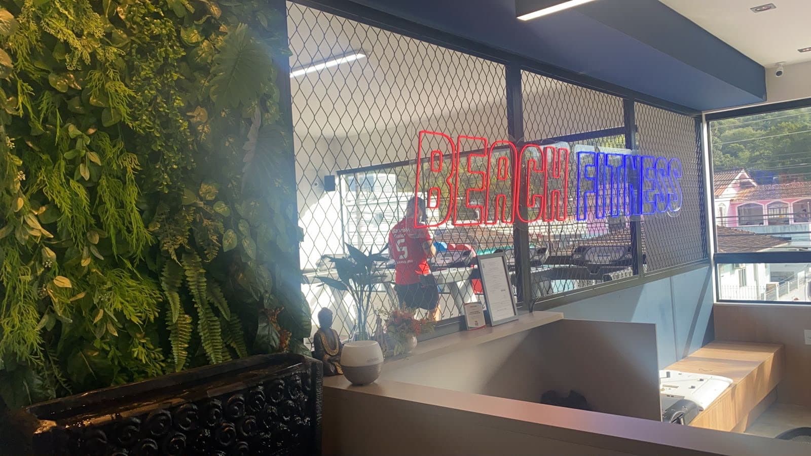 Marca Beach Fitness aplicada no vidro da recepção, com a academia ao fundo