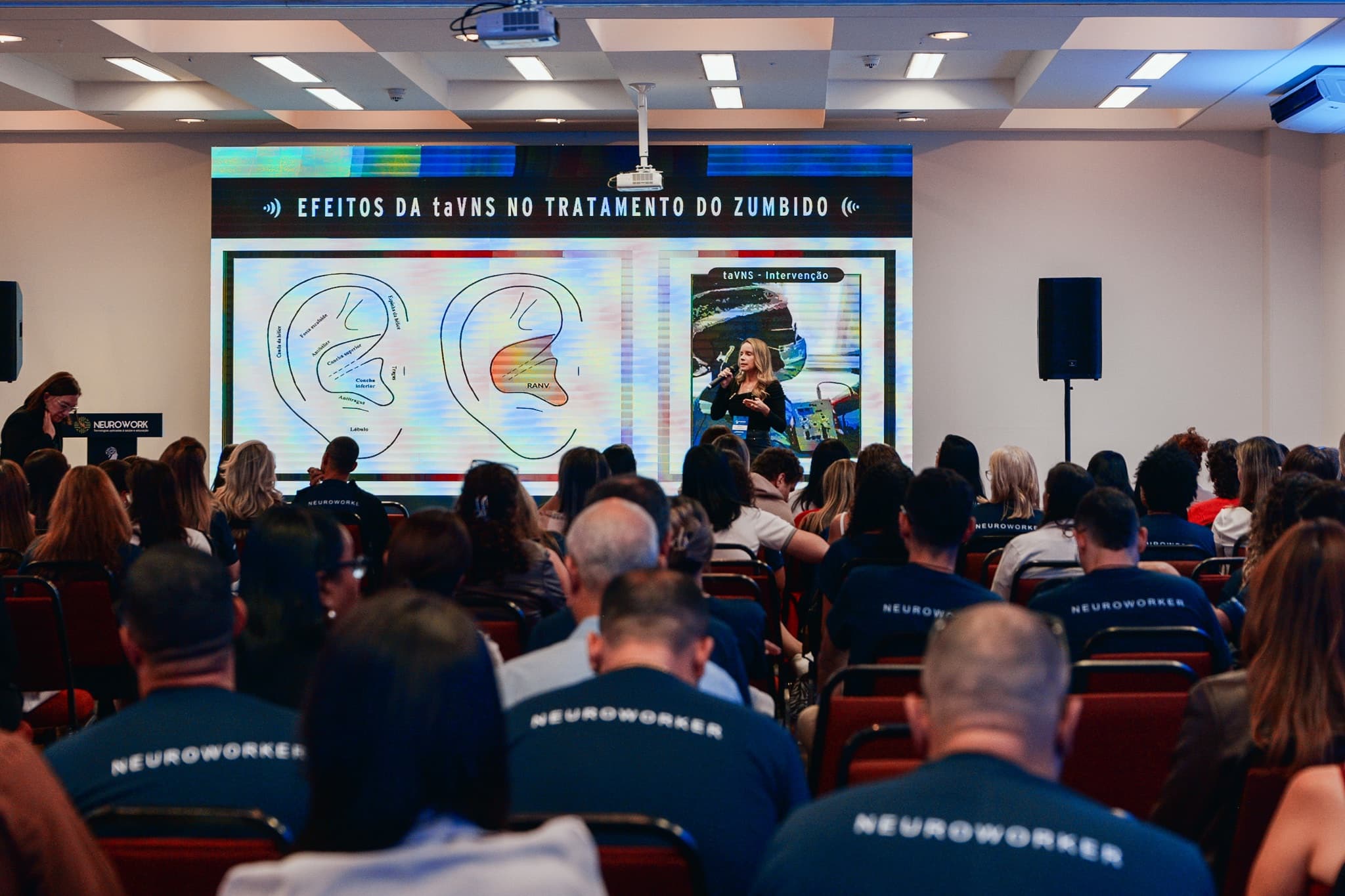 Detalhe da produção do CONTASE: bancada de operação com os equipamentos de som e o banner do evento ao fundo
