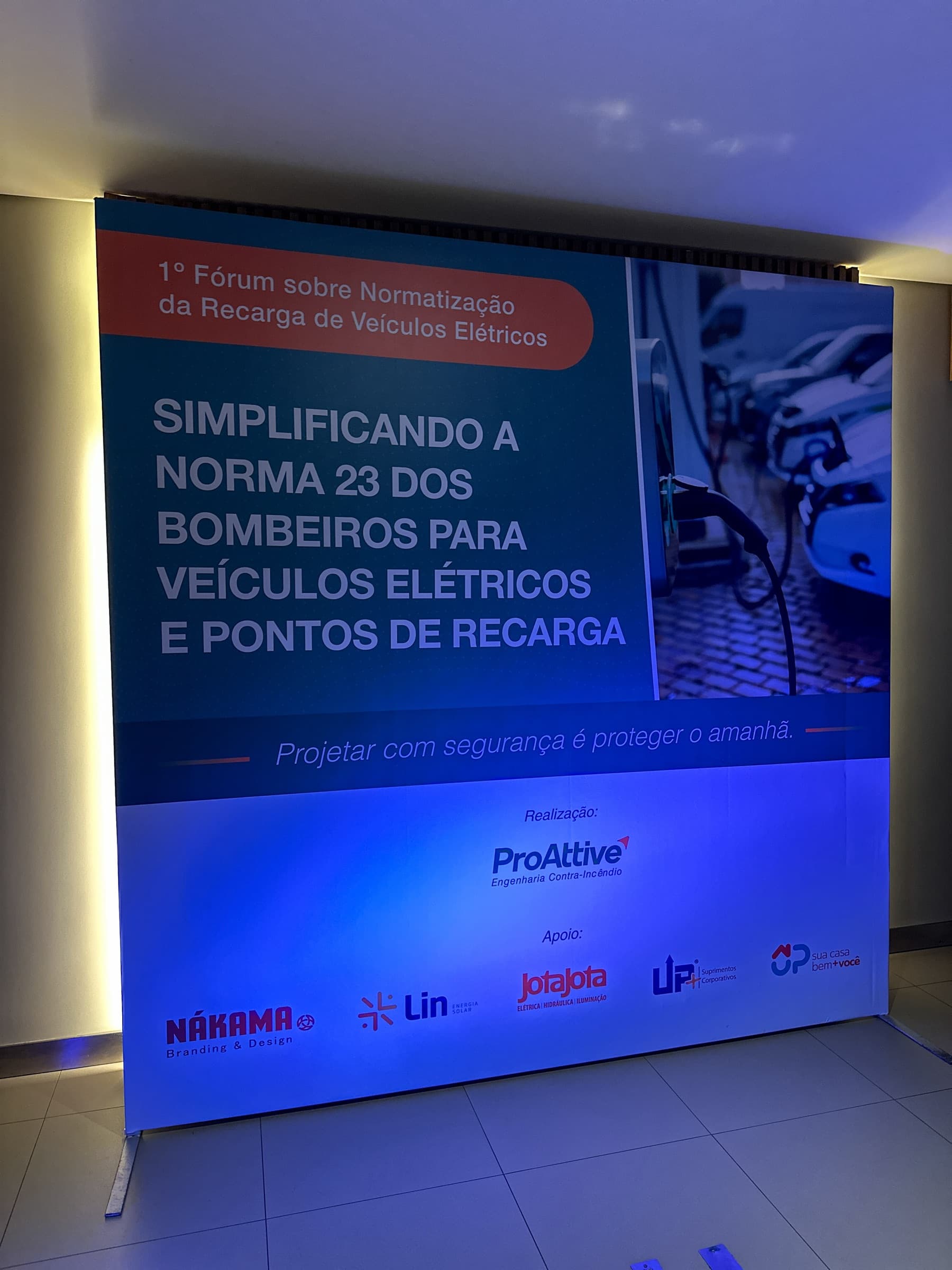 Painel de fundo do evento com o tema Simplificando a norma 23 dos bombeiros para veículos elétricos e pontos de recarga