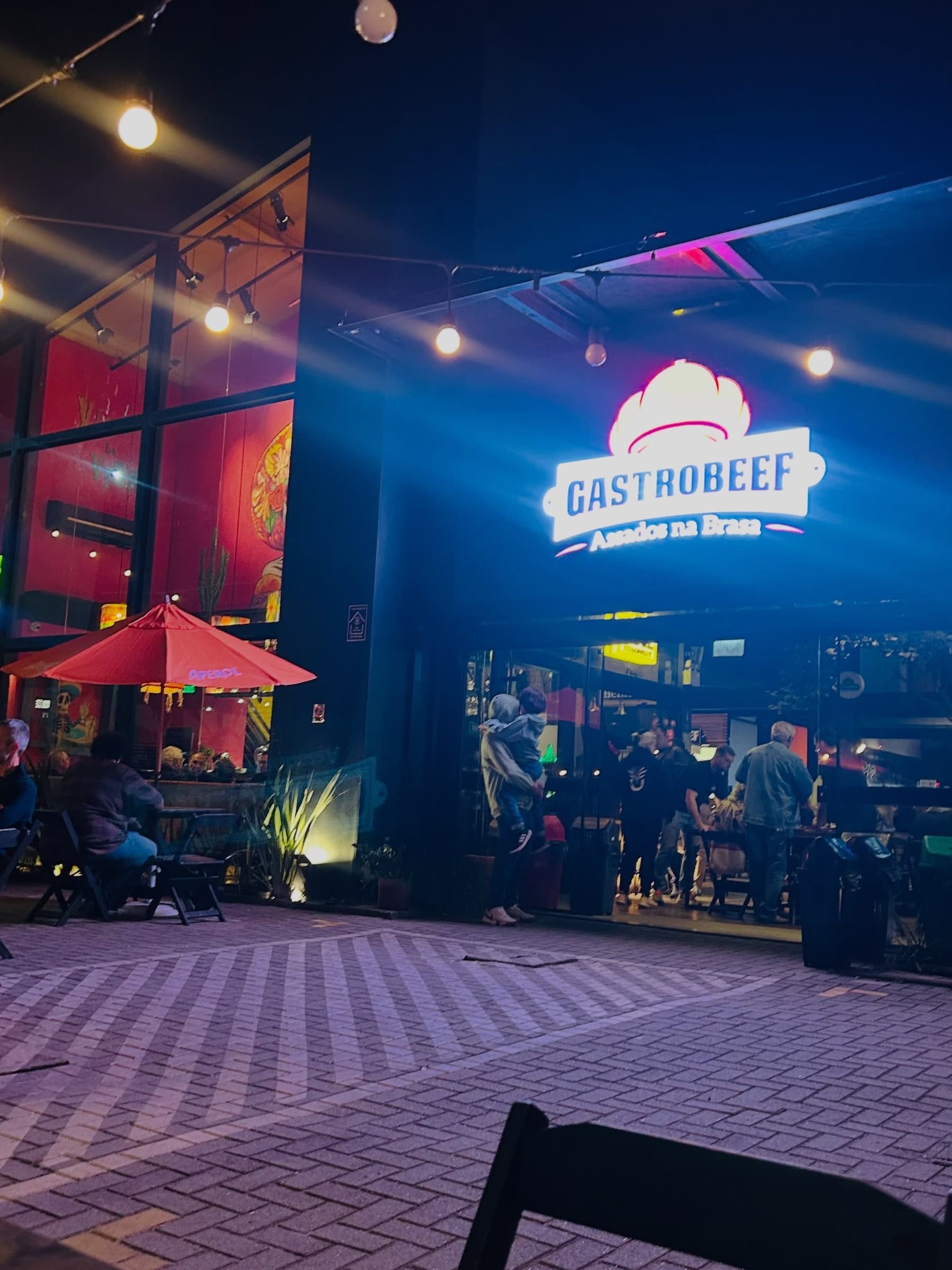 Fachada do restaurante GastroBeef à noite, com o letreiro iluminado e o salão aceso