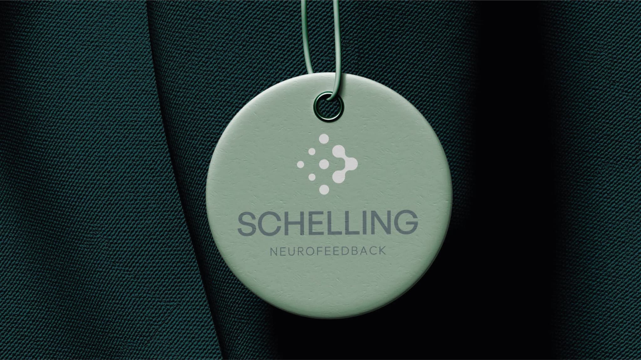 Tag circular com a marca Schelling Neurofeedback pendurada em tecido escuro